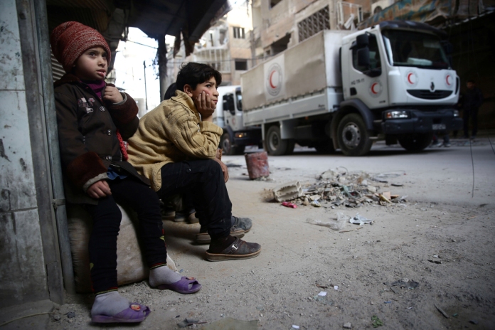 Children watch as an aid convoy of Syrian Arab Red Crescent drives through the besieged town of Douma